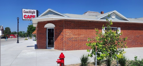 Exterior of Coachlight Café, a brick building with a sign, surrounded by greenery and a fire hydrant. Clear blue sky.