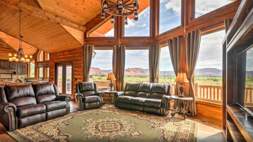 Cozy log cabin living room with large windows, mountain views, and elegant furnishings.