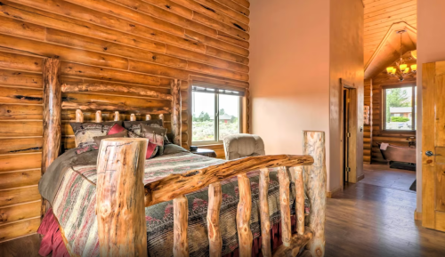 Cozy log cabin bedroom featuring a wooden bed, rustic decor, and large windows with natural light.