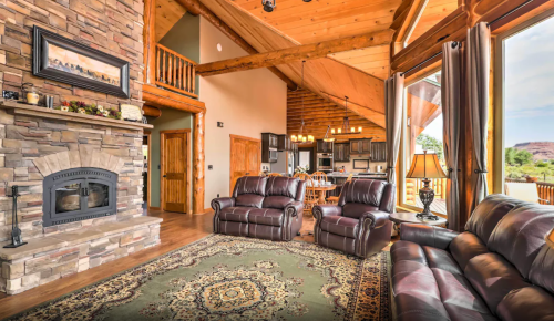 Cozy living room with stone fireplace, leather recliners, and large windows showcasing a scenic view.