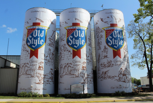 Three large silos adorned with "Old Style" beer branding and illustrations, set against a clear blue sky.