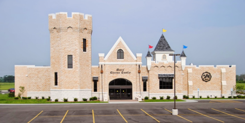 A large, castle-like building with towers and colorful flags, set against a clear sky and parking lot.