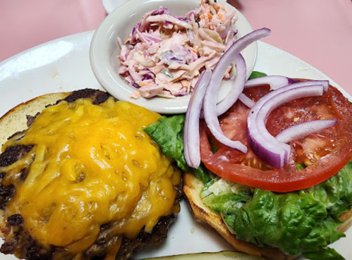 A cheeseburger with melted cheddar, lettuce, tomato, and onion, served with a side of coleslaw on a plate.