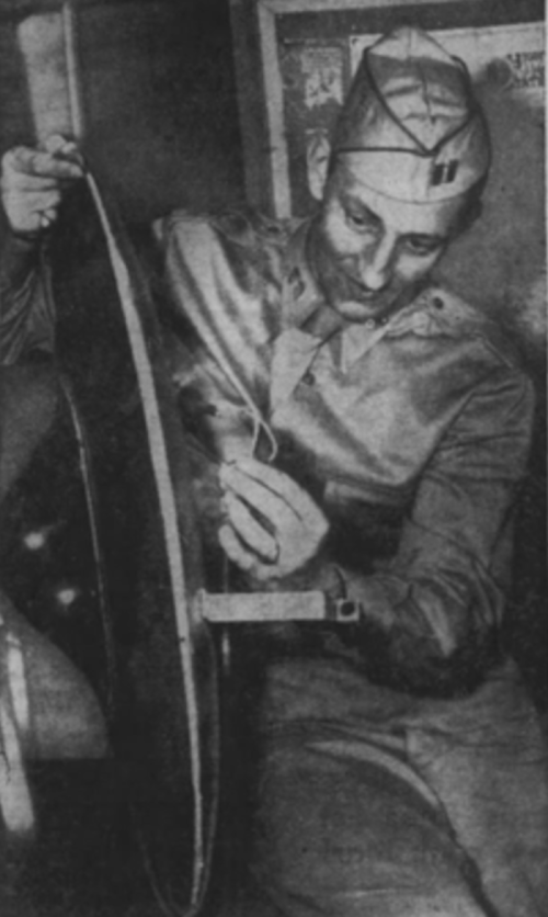 A man in military uniform examines a circular object, focused on a small detail, in a dimly lit environment.