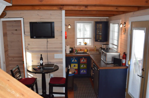 Cozy kitchen and dining area in a small cabin, featuring wooden walls, a table, and modern appliances.