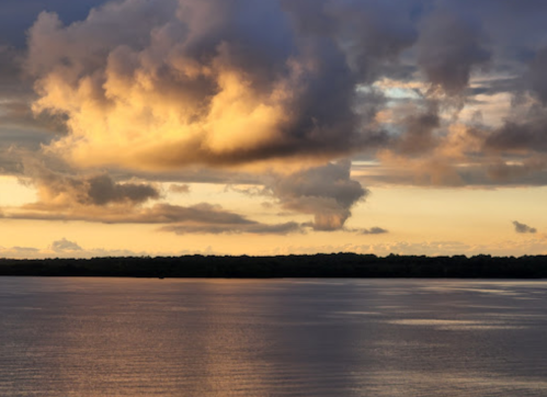 A serene sunset over a calm lake, with vibrant clouds reflecting warm colors in the water.