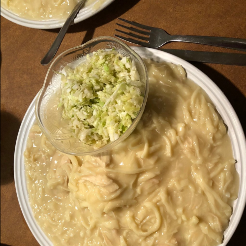 A plate of creamy pasta with a side of shredded lettuce in a bowl, set on a wooden table with utensils.
