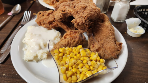 A plate of fried chicken with mashed potatoes and gravy, served with a side of corn.