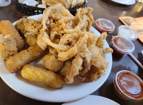 A plate of fried food including onion rings, corn fritters, and dipping sauces.