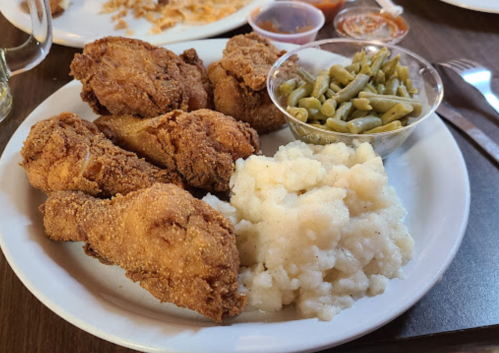 A plate of fried chicken, creamy mashed potatoes, and green beans served with dipping sauces.