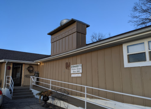 Exterior of a building with a sign reading "Gerhardt's Chicken Dinner" and a sloped roof under a clear blue sky.