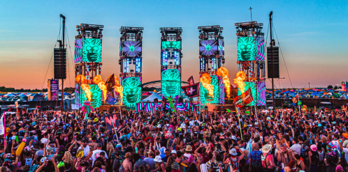 A vibrant music festival scene with a large crowd, colorful stage lights, and a sunset backdrop.