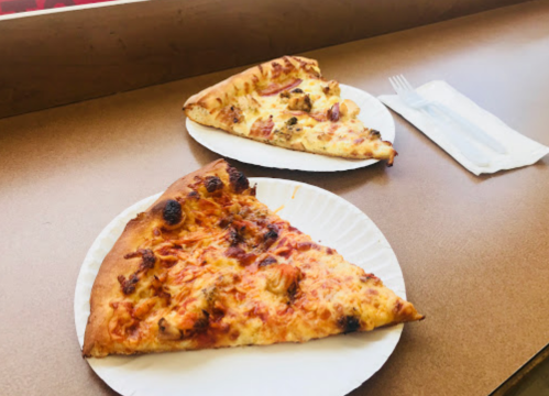 Two slices of pizza on paper plates, one with toppings and the other plain, on a wooden table.