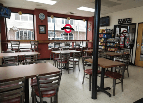 Empty diner interior with wooden tables, chairs, and a snack display, featuring a large window with a logo.
