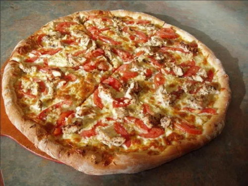 A large pizza topped with cheese, sliced tomatoes, and pieces of chicken on a golden crust.