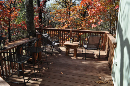 A wooden deck surrounded by colorful autumn trees, featuring a small table and four chairs.