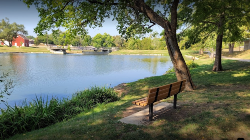 A serene park scene featuring a bench by a calm pond, surrounded by trees and greenery.