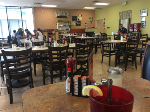 A mostly empty restaurant with tables, chairs, and a counter; a drink with a lemon slice is in the foreground.