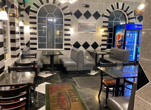 Interior of a pizza restaurant featuring black and white tiled walls, tables, booths, and a soda vending machine.