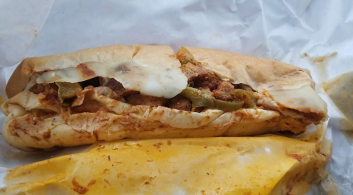 A close-up of a sandwich filled with meat, cheese, and peppers, resting on crumpled white paper.