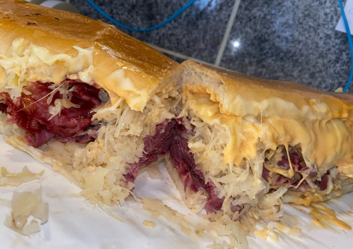 A close-up of a sandwich filled with corned beef, sauerkraut, and melted cheese on a soft bun.