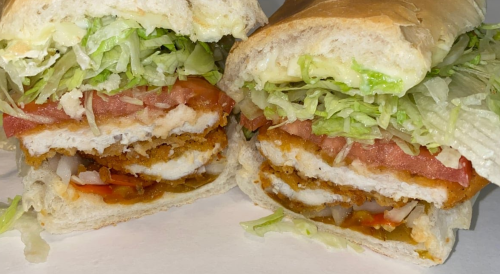 A close-up of a sandwich filled with fried chicken, lettuce, tomato, and sauce, served in a soft bun.