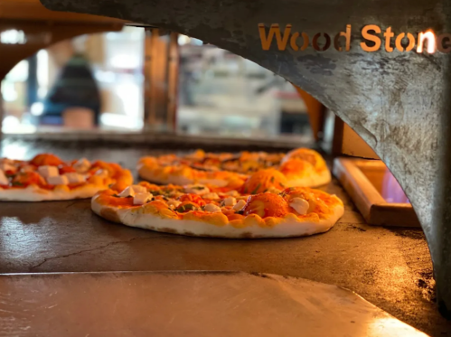 Three pizzas baking in a wood-fired oven, with a warm glow illuminating the crusts.