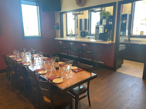 A dining area with a long table set for a meal, featuring glasses and plates, and a bar in the background.