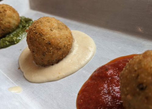 Three golden-brown croquettes on a tray, accompanied by green, white, and red sauces.