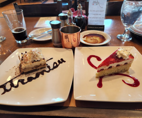 Two dessert plates: one with a layered cake topped with whipped cream and the other with a strawberry cheesecake drizzled with sauce.
