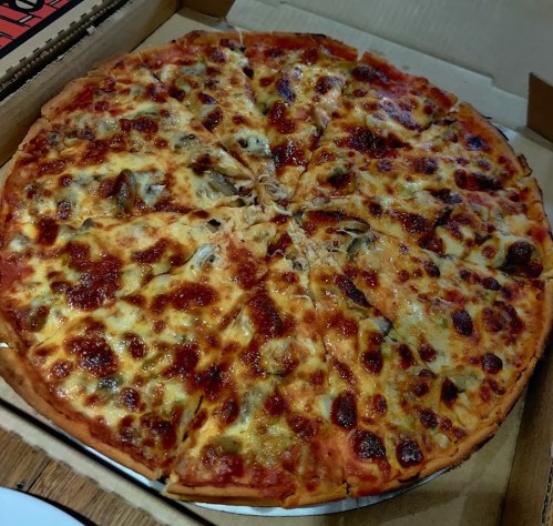 A large pizza with melted cheese, pepperoni, and toppings, cut into slices, in a pizza box.