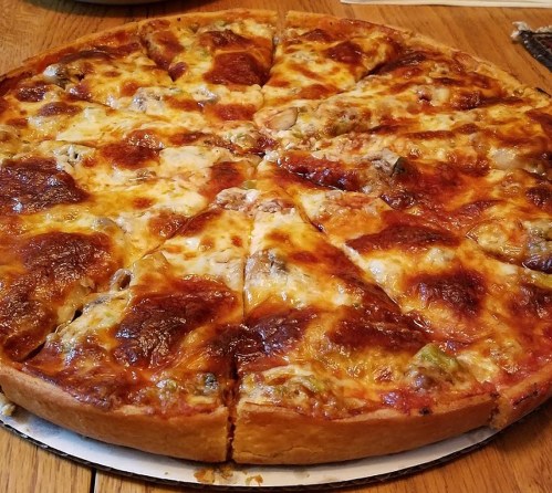 A freshly baked pizza with melted cheese and various toppings, sliced into equal pieces on a wooden table.