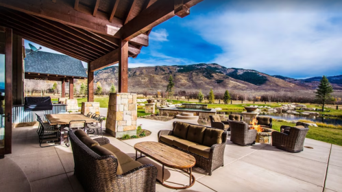 A scenic outdoor patio with seating, a fire pit, and a view of mountains and a pond in the background.