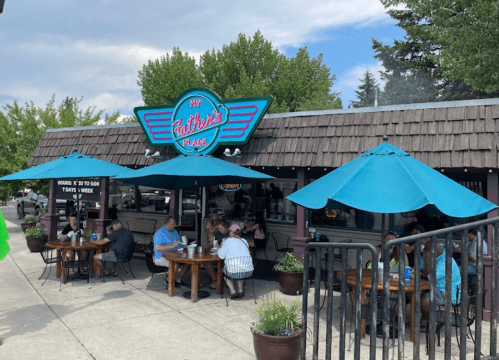 A restaurant with a blue awning and outdoor seating, featuring diners enjoying meals under large umbrellas.