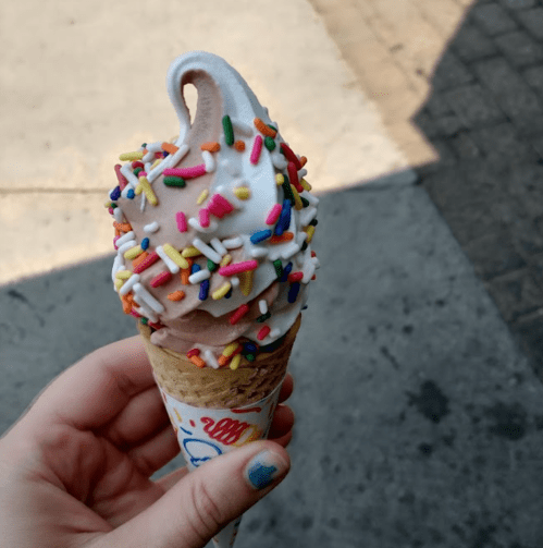 A hand holding a cone of soft-serve ice cream topped with colorful sprinkles.