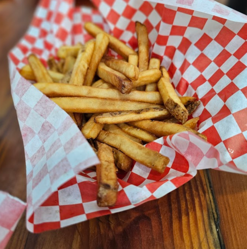 A basket of golden-brown French fries lined with red and white checkered paper on a wooden table.