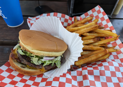 A burger with lettuce and onions on a paper-lined tray, accompanied by a side of golden fries and a blue drink.