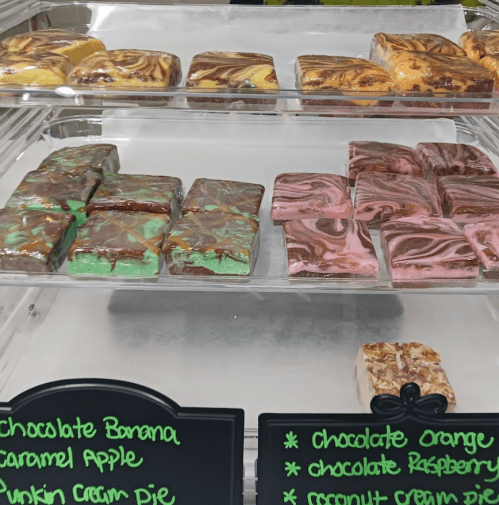 A display case filled with colorful fudge squares, labeled with various flavors like chocolate banana and pumpkin cream pie.