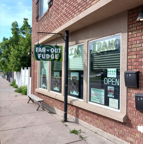 A brick storefront with a sign reading "Far-Out Fudge" and large windows displaying various treats.