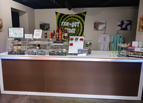 A colorful dessert shop counter with various treats displayed, a tie-dye banner, and merchandise hanging on the wall.