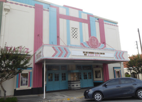 A colorful vintage theater with pink and blue exterior, featuring a marquee and parked car in front.