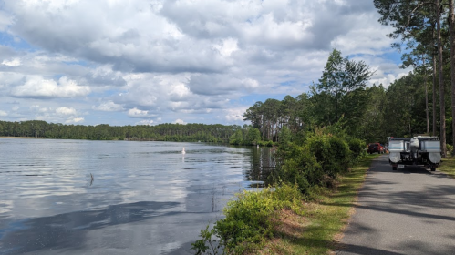 A serene lakeside view with a winding path, trees, and a boat parked nearby under a cloudy sky.