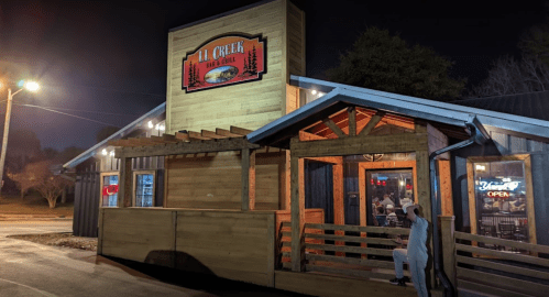 A rustic restaurant exterior at night, featuring wooden architecture and a welcoming sign.