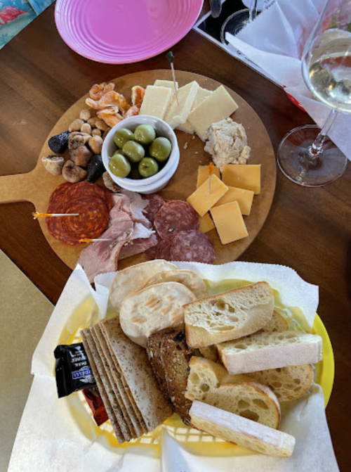 A wooden platter with assorted cheeses, meats, olives, nuts, and a side of bread on a yellow plate.