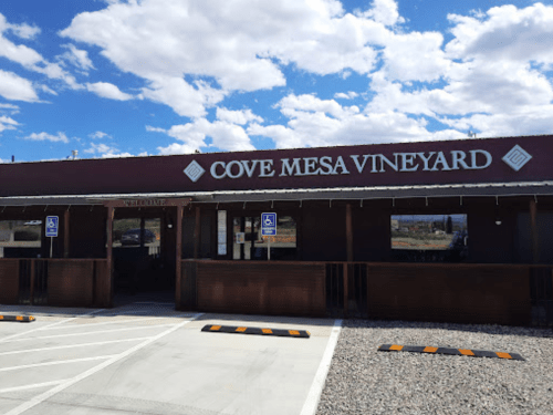 Exterior of Cove Mesa Vineyard with a welcoming sign and blue sky in the background. Accessible parking visible.
