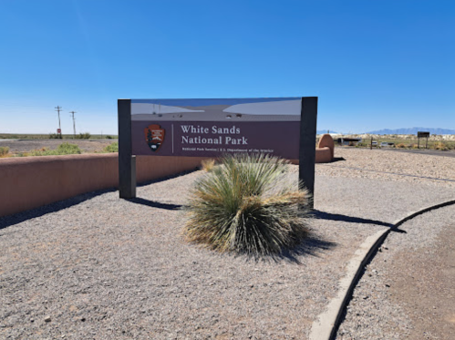 Sign for White Sands National Park, surrounded by desert landscape and clear blue sky.