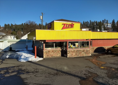 A bright yellow and red fast-food restaurant with a stone facade, surrounded by snow and trees in the background.