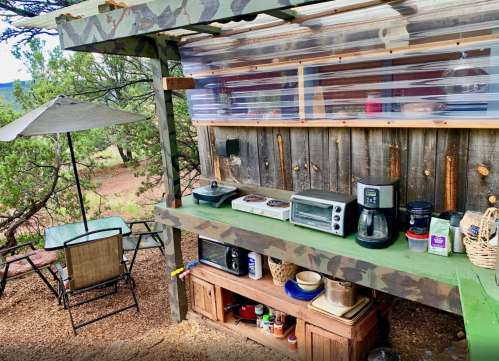 Outdoor kitchen with camouflage decor, featuring a countertop, appliances, and a shaded seating area nearby.