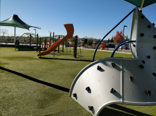 A colorful playground with climbing structures, slides, and a grassy area under a clear blue sky.