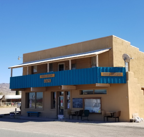 A small, rustic grocery store and café with a blue awning, located in a desert setting.